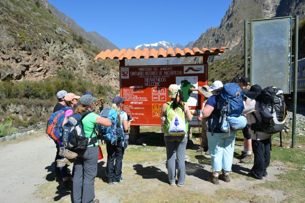 Grupo de caminantes con mochilas frente al panel de bienvenida del Santuario Histórico de Machupicchu, en el ingreso a la Red de Caminos Inka