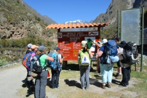 Grupo de caminantes con mochilas frente al panel de bienvenida del Santuario Histórico de Machupicchu, en el ingreso a la Red de Caminos Inka