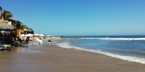 Orilla de la playa de Máncora con bañistas, surfistas y quinchos frente al mar