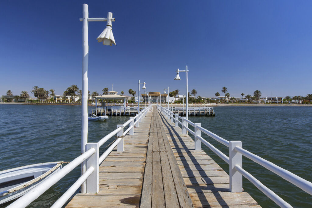Muelle de madera con barandas blancas frente a un hotel en la bahía de Paracas